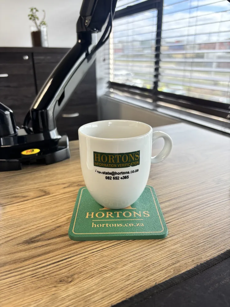 Green coaster with gold company branding under a coffee mug on an office desk